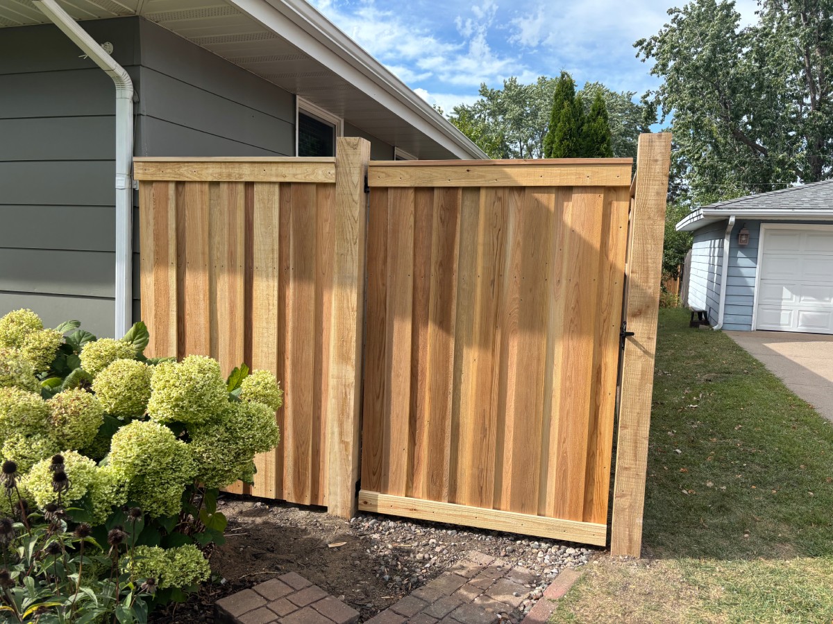 Close-up of wood privacy fence with gate post and cap, next to house siding