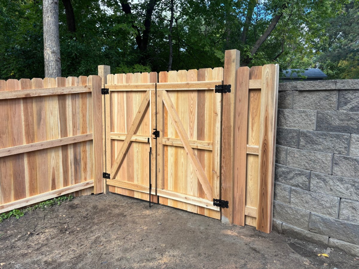 Cedar double gate with X-brace design and black hinges beside stone wall