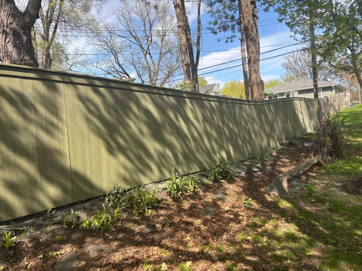 Green painted cedar privacy fence bordering mulched garden bed under trees