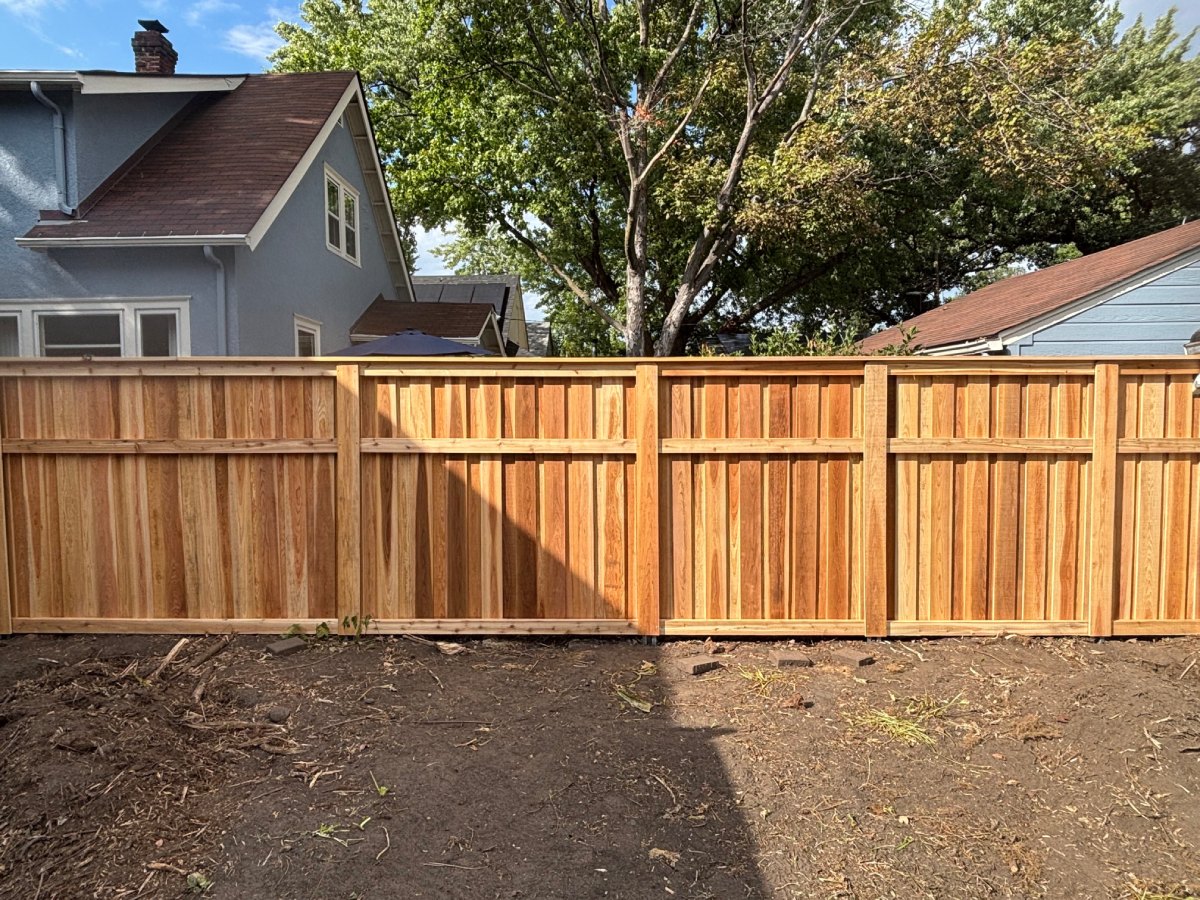 Wood privacy fence installed along backyard property line with mature trees in background