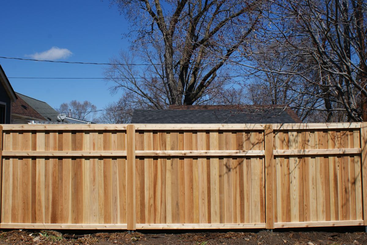 Cedar privacy fence panels installed in a Roseville, MN backyard with bare trees and blue sky in the background