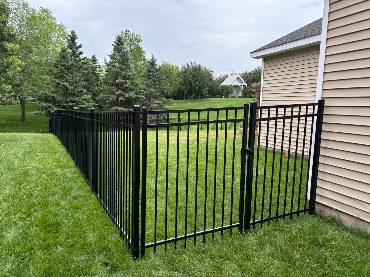 Black ornamental steel fence with a walk gate along a green lawn